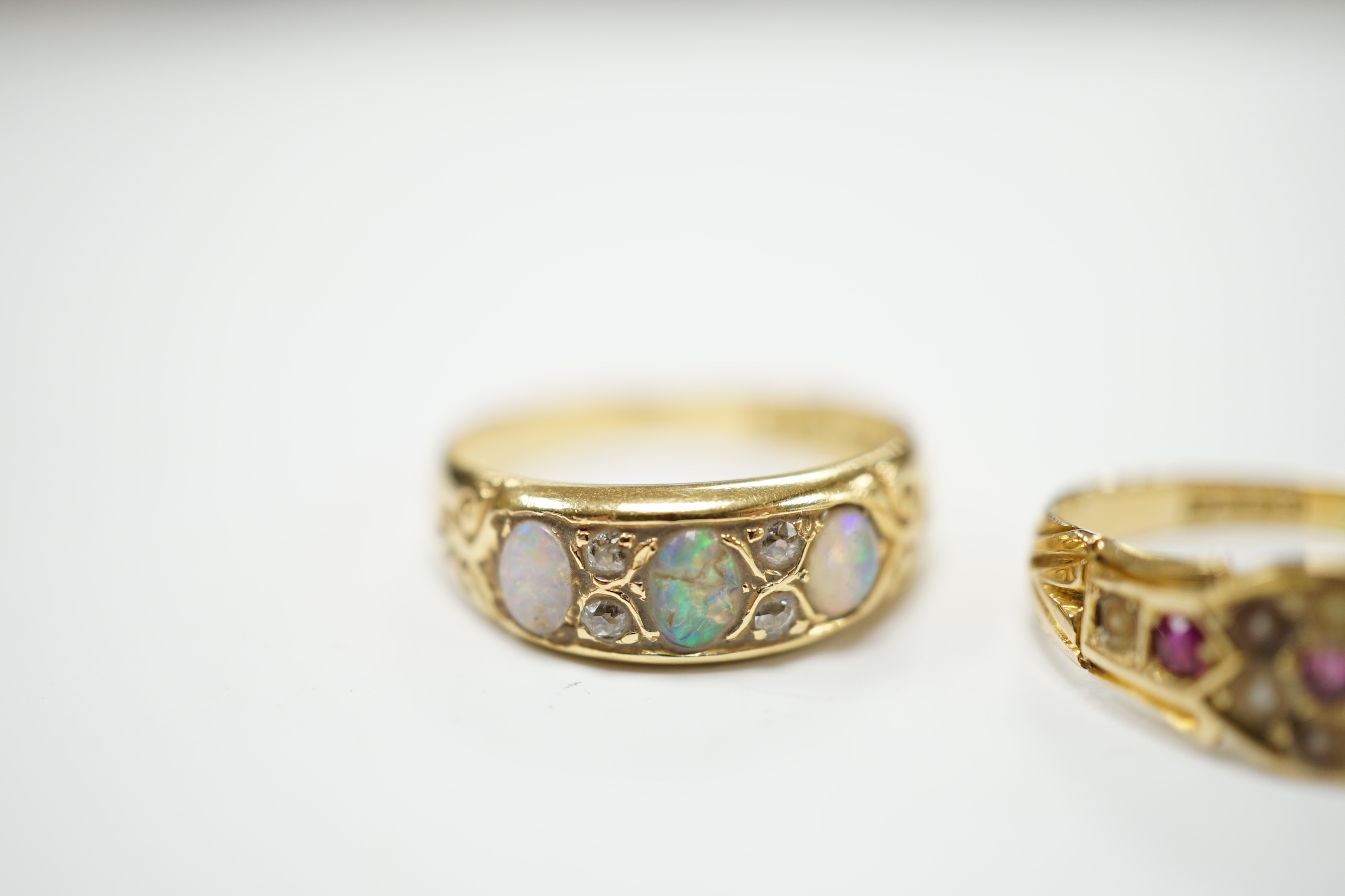 A late Victorian 18ct gold and three stone white opal set half hoop ring, with diamond chip spacers, size M (opal chipped), together with a similar 18ct gold, ruby and seed pearl ring, size K/L, gross weight 5.7 grams.